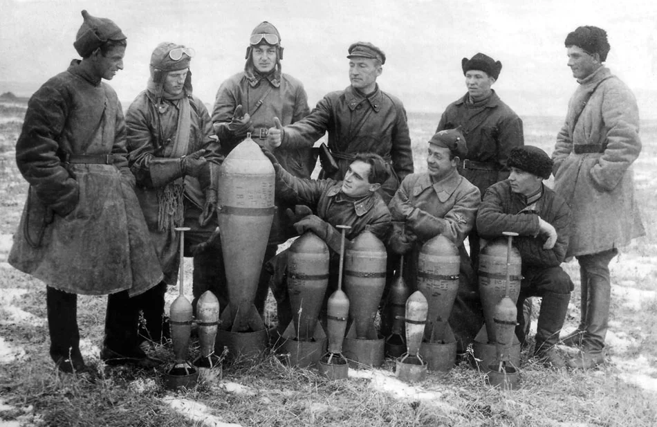 Советские авиаторы позируют на аэродроме с фугасными бомбами АВ-32, АФ-82 и осколочными ОФ-8 ...webp
